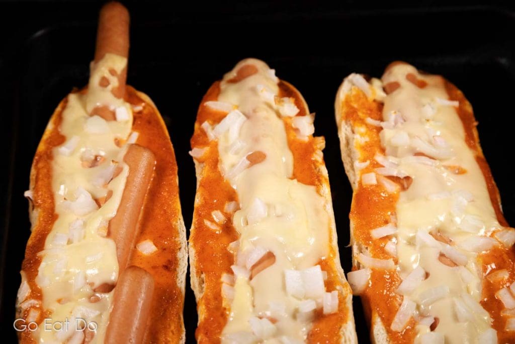 Hot dogs in a baguette overbaked with cheese and chopped onions.