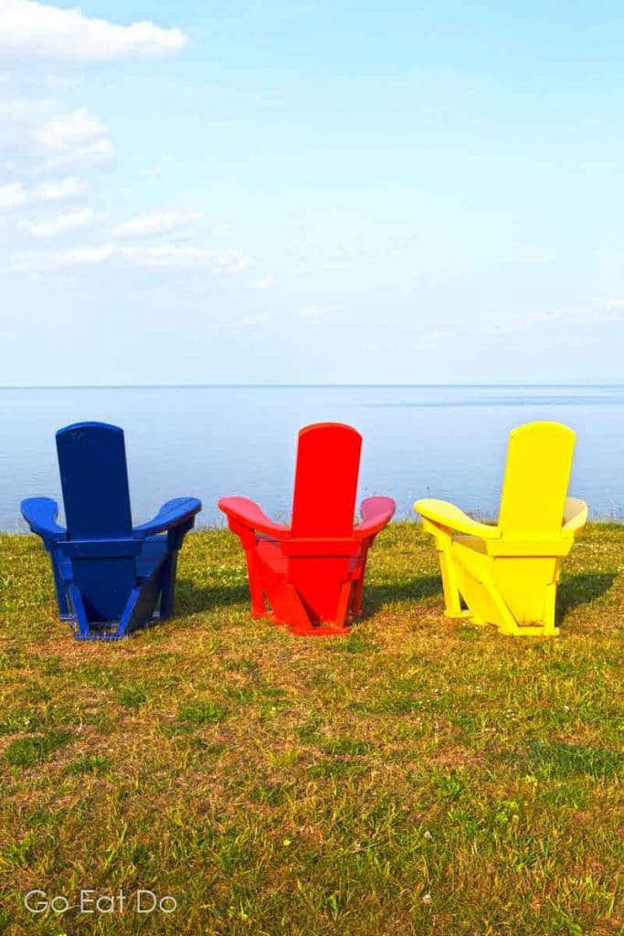 Adirondack chairs in the primary colours overlooking the Atlantic Ocean, whose coastline provides opportunities for photography in Nova Scotia, Canada.