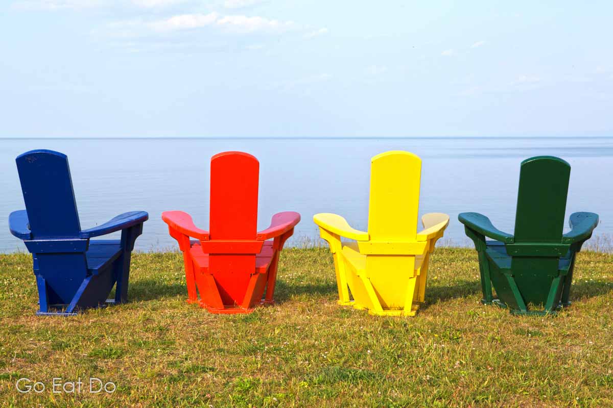 Blue, red, yellow and green Adirondack chairs overlooking the Atlantic Ocean on Nova Scotia's Northumberland Shore.