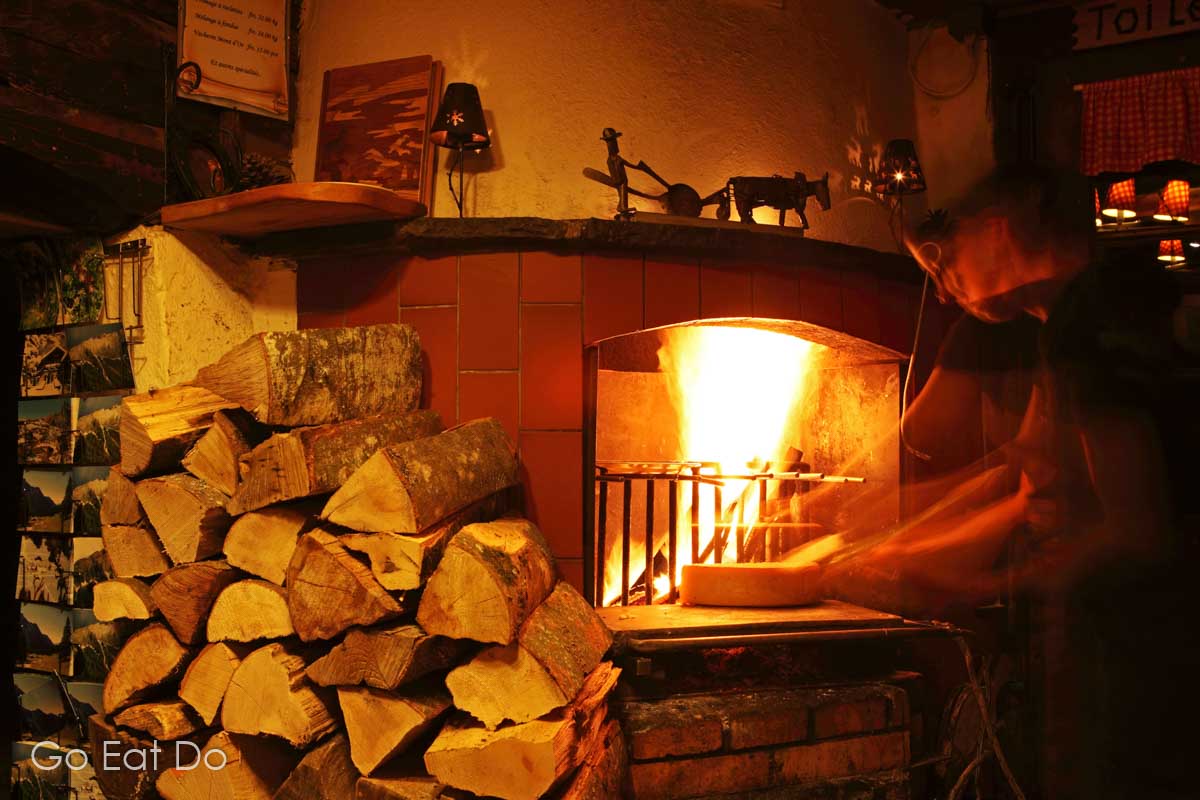 Ideal cuisine during winter in Switzerland. Raclette being prepared by an open fire in the cosy Refuge de Solalex restaurant near Villars, Switzerland.