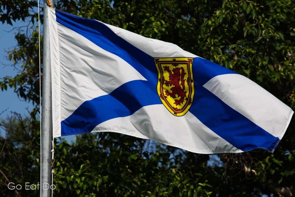 The flag of Nova Scotia featuring the cross of Saint Andrew and lion rampant. It flies on a sunny day at Burntcoat Head Park, a place worth visiting while exploring Nova Scotia beyond Halifax.