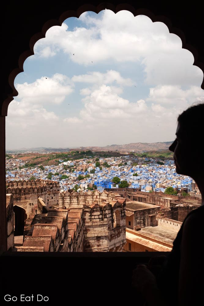 A woman looks out over Jodhpur the blue city of India and towers of Mehrangarh Fort from one of the windows of the historic fortress.