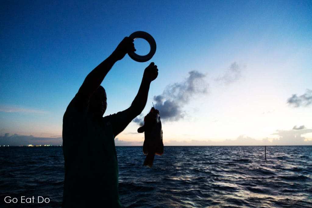 A fisherman holds up a fish caught using a line and reel on a night fishing expedition in the Maldives