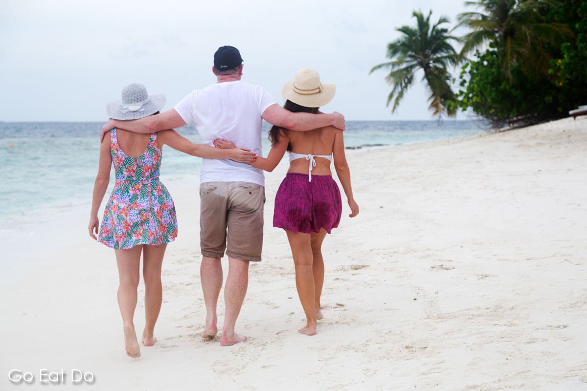 Man and two women walking along a beach on an island resort in the Maldives