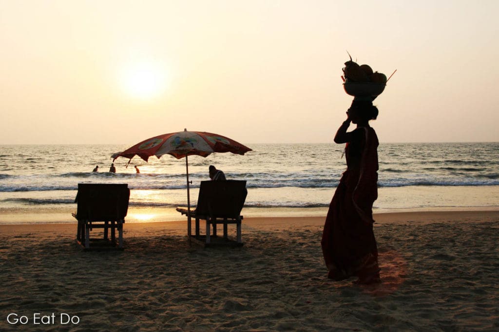Indian woman walks along a beach washed by the Arabian Sea as the sun sets in Goa, India.