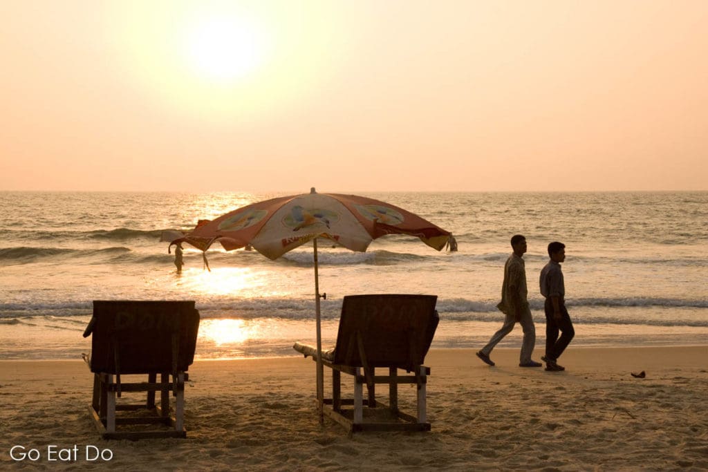 People walking on a Goan beach as the sun sets.