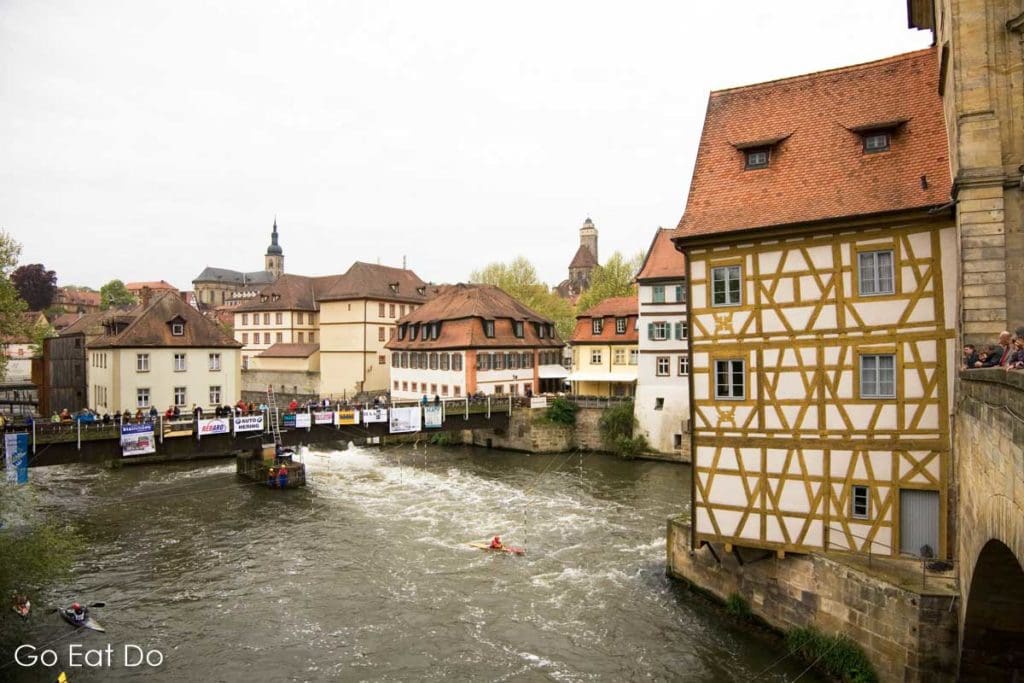 Kayakers paddle past the Rathaus (Town Hall) of Bamberg, which is built over the River Regnitz. The city hosts the Gustav Mahler Conducting Competition.