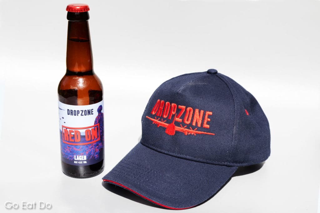 Bottle of DropZone Brewery's Red On beer and a baseball cap bearing the brewery's logo.