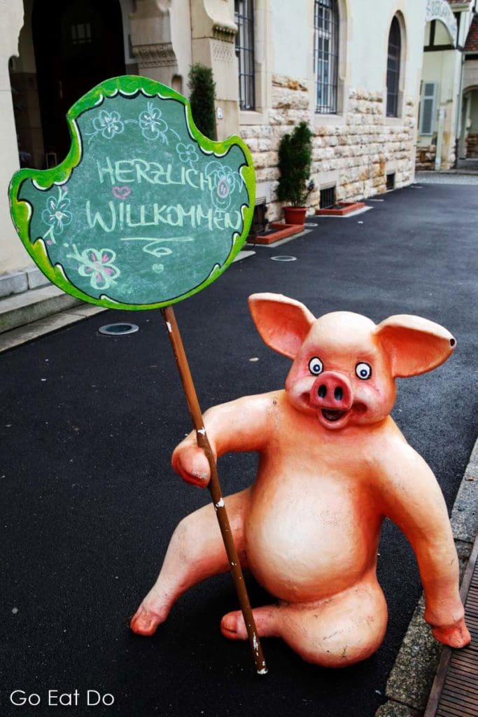 A pink piglet holding a chalkboard sign wishing a hearty welcome to visitors to the SchweineMuseum Stuttgart.