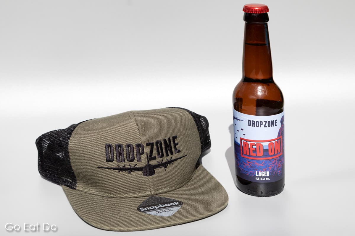 Snapback cap bearing the DropZone Brewery logo next to a bottle of Red On beer.
