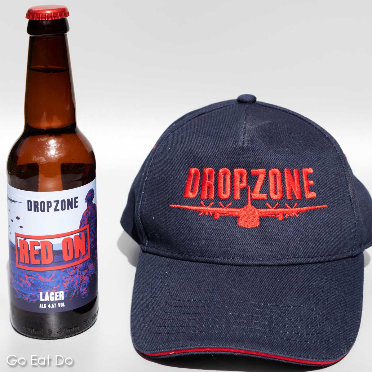 A bottle of DropZone Brewery's Red On beer next to a baseball cap.