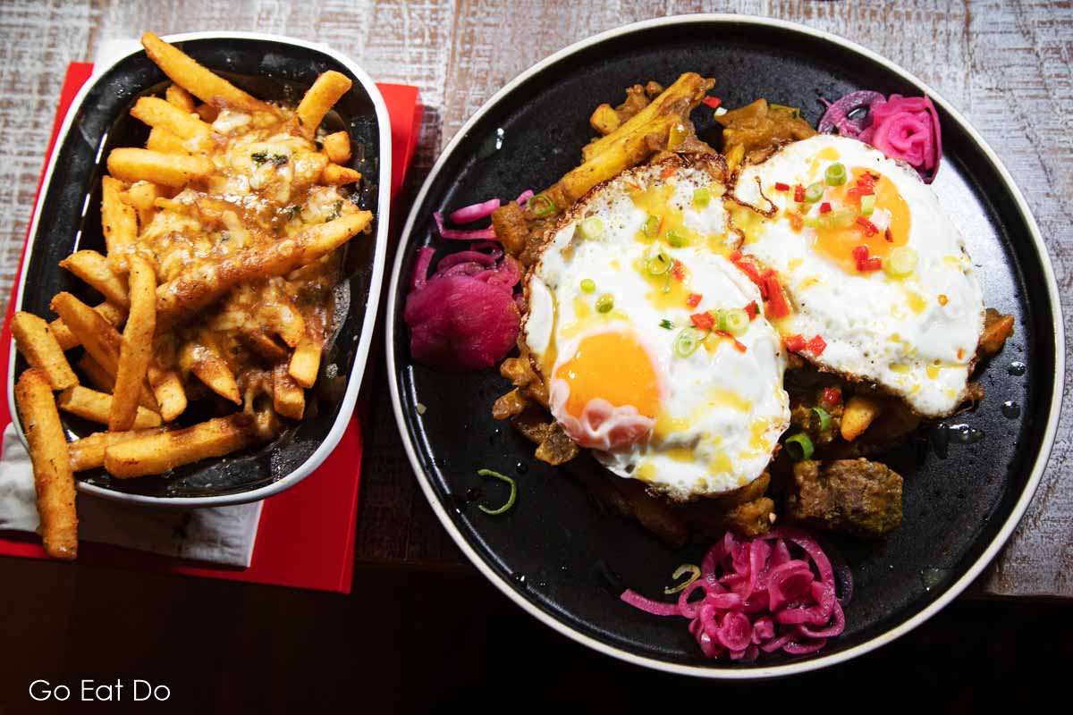 Goat curry hash topped with two fried eggs and a side of cheesy jerk fries.