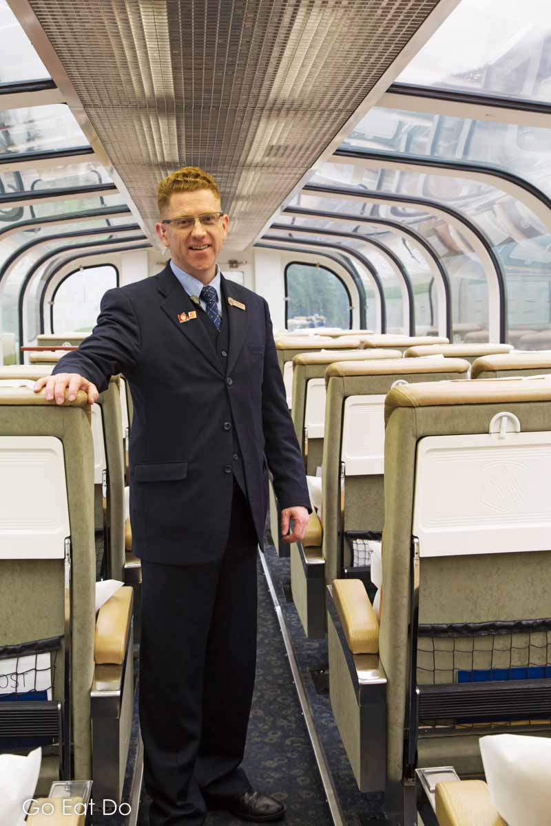 Train manager Zebulon Fastabend standing in the upper level of one of the Rocky Mountaineer's GoldLeaf Service cars.