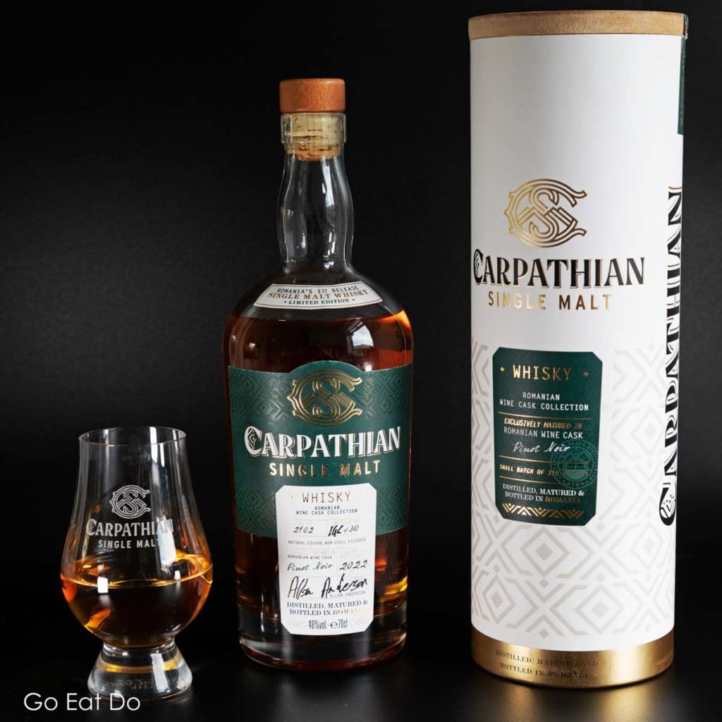 A glass of Carpathian Single Malt whisky with a bottle and presentation pack.