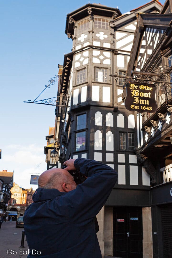 A visitor to Chester photographs the half-timbered facades of historic buildings.