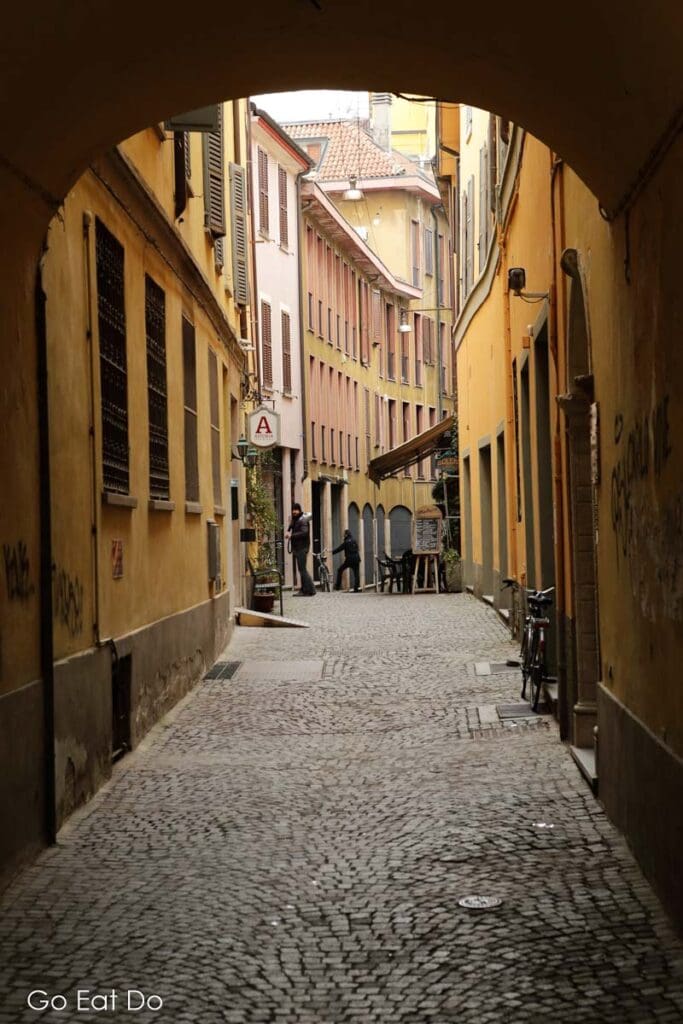 Pastel coloured houses face onto a cobbled alley in Cremona, Italy.