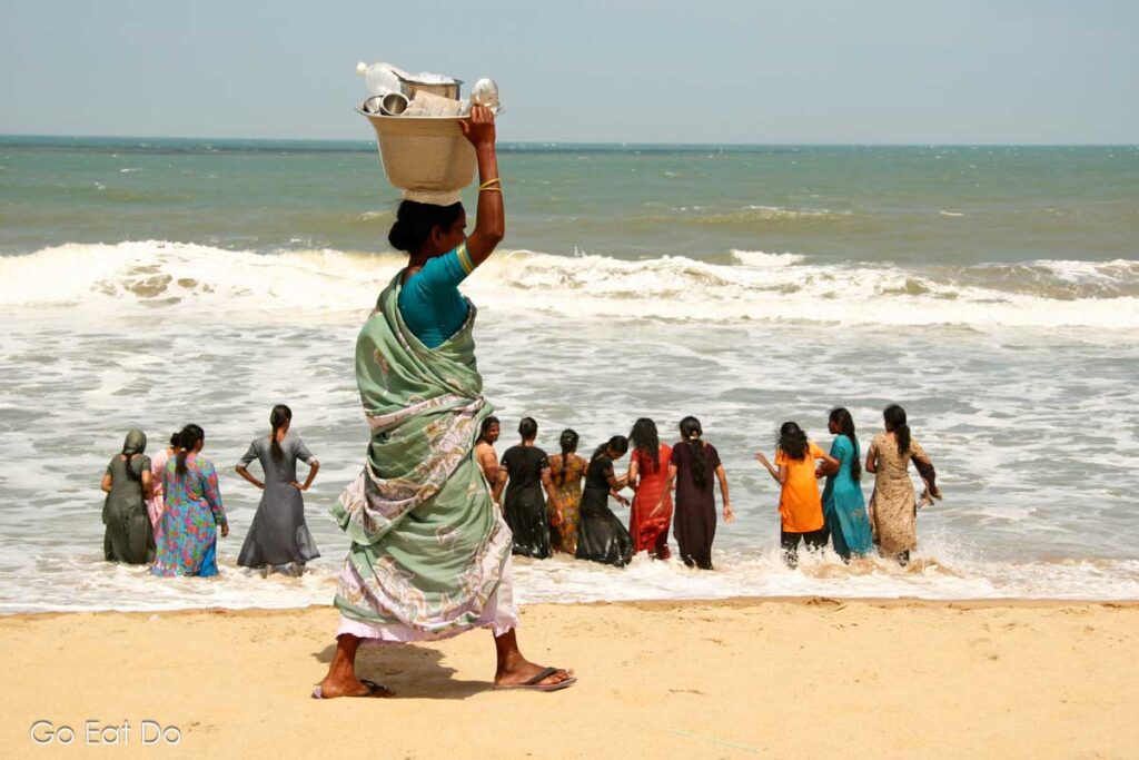 Women bathing in the Bay of Bengal while a woman walks on Mahabalipuram Beach.